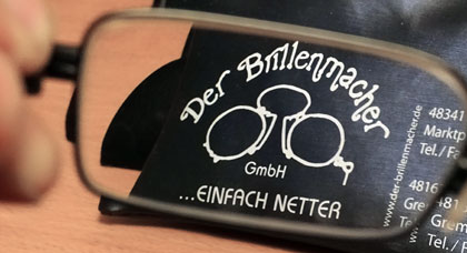 Das Bild zeigt durch ein Brillenglas das Logo eines Optikers mit dem Slogan 