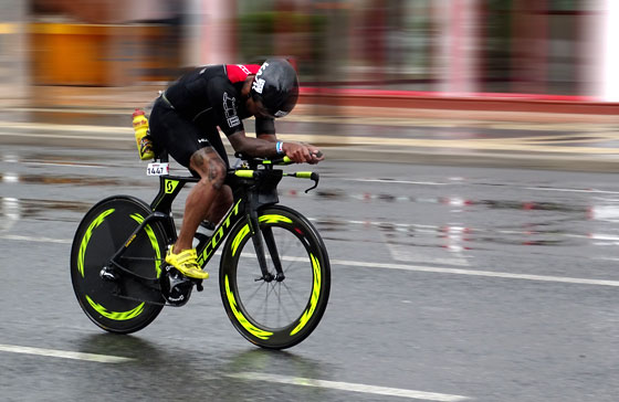 Ein Rennradfahrer mit Helm im Regen auf einer Straße beim Ironman-Wettkampf.