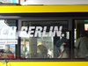 Ein Berlinschriftzug in weiß auf einer Busfensterscheibe.Im Bus sitzen mehrere Personen.