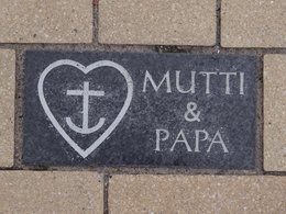 Ein dunkler Bodenstein mit der Gravur Mama und Papa, einem Herz und einem Anker.