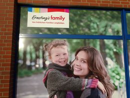 Ein Werbeplakat des Geschäftes Erstings family mit einer Mutter, die ein Mädchen auf dem Arm hat.