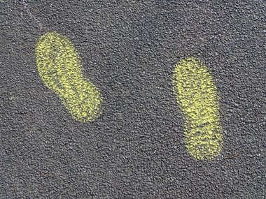 Ein mit gelber Kreide auf den Straßenbelag aufgemalter Fußabdruck von zwei Füßen in Schrittstellung.