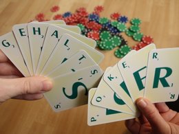 Zwei Hände halten gefächerte Karten mit Buchstaben, die das Wort Gehaltspoker ergeben und im Hintergrund liegen verschwommene Pokerchips auf dem Tisch.