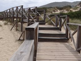 Eine leicht aufsteigende Holztreppe über einer Sandlandschaft.