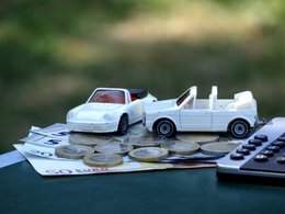 Scheine, Münzen, ein weißer Porsche und ein Golf-Cabriolet mit einem Taschenrechner.