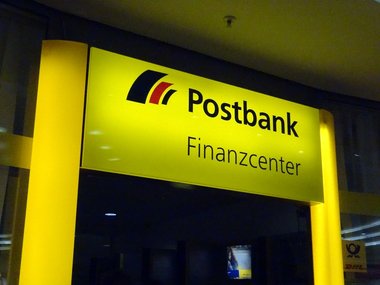 Ein gelb leuchtender Eingang von einem Finanzcenter der Postbank.