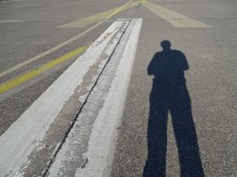 Der Schatten einer Person auf einer Flughafenrollbahn.