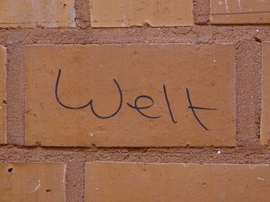  Rote Ziegelsteinmauer in einer Turnhallenkabine auf dem das Wort Welt geschrieben steht.