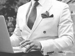 Ein Mann im weißen Anzug mit gepunkteter Krawatte arbeitet an einem Notebook.