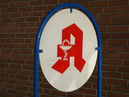 Ein rundes Apothekenschild mit dem roten Symbol und einer blauen Halterung.