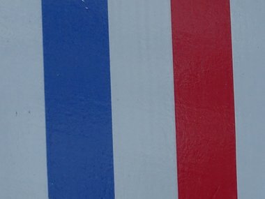 Die Fahne von Frankreich und der Ort Amilly auf einem weißen Schild an einer roten Backsteinwand.