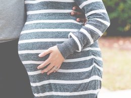 Der Babybauch einer schwangeren Frau im gestreiften Kleid.