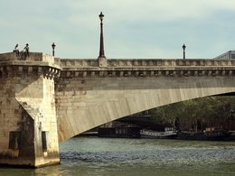 Eine historische Brücke über einem Fluß mit Langbooten im Hintergrund.