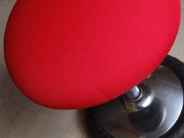 Ein Bürostuhl mit roter Sitzfläche, als Hocker.