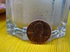 Eine englische Münze von 1996 lehnt an einem leeren Kaffeeglas mit der Aufschrift: in god we trust.