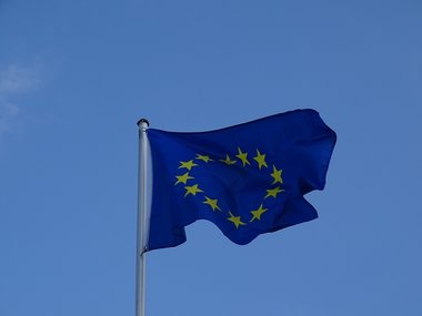 Die Flagge der Europäischen Union flattert vor blauem Himmel bei Sonnenschein im Wind.