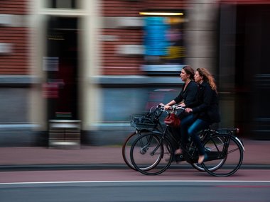 Zwei Frauen fahren auf dem Fahrrad eine Straße entlang.