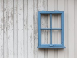 Ein blauer Fensterrahmen als Dekoration an einer weißen Wand.