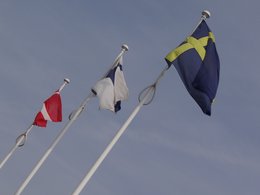 Drei Länderflagge vor blauem Himmel schräg aufgenommen mit ihren weißen Masten.