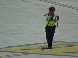 Eine Frau mit Kopfhöreren und neongelber Sicherheitsweste vom Flughafenbodenpersonal.