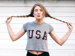 Eine amerikanische Studentin mit Zöpfen und USA-Shirt gibt dem Fotografen einen Kuß.