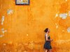 Eine Frau geht an einer orangenen Wand mit einem spanischen Straßenschild entlang.