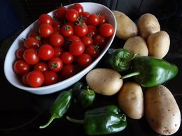 Tomaten in einer Schale, grüne Paprika und Kartoffeln liegen zusammen auf einem schwarzen Untergrund.