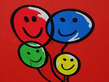Bild mit einem grünen, einem gelben, einem blauen und einem roten Luftballon mit lachenden Gesichtern. Alle Linien sind schwarz und komplette Hintergrund ist rot.