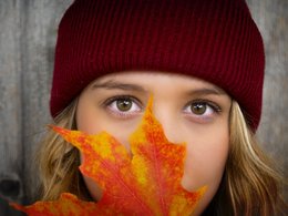 Eine Frau schaut mit ihren Augen über ein Blatt Herbstlaub.
