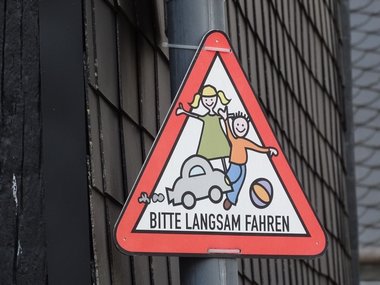 Ein Schild mit gemalten, spielenden Kindern und dem Text: Bitte langsam fahren.