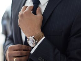 Ein Manager im Anzug und mit einer teuren Uhr am Arm richtet sich seine Krawatte.