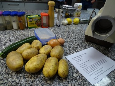 Ein Rezept für Zucchini-Kartoffel-Röstis liegt auf einer Arbeitsfläche mit entsprechenden Zutaten.