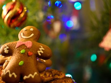 Ein Lebkuchenmännchen mit Zuckerguß und ein Weihnachtbaum im Hintergrund.
