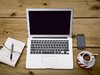 Mobiles Arbeiten zuhause am macbook mit Kaffee. Ein Laptop, ein Glas Wasser, ein Notizbuch und ein Sift auf einem Tisch.