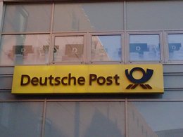 Der gelbe Banner der deutschen Post mit dem entsprechenden Logo an einer Gebäudefassade.