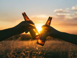 Zwei Freunde stoßen bei Sonnenuntergang mit ihren Flasche Bier an.