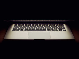 Das Bild zeigt eine vom dreiviertel zugeklappten Monitor beleuchtete Notebooktastatur, komplett umgeben von Dunkelheit und symbolisiert das Thema Ransomware-Angriff. 