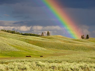 Ein Regenbogen über einer hügeligen Landschaft.