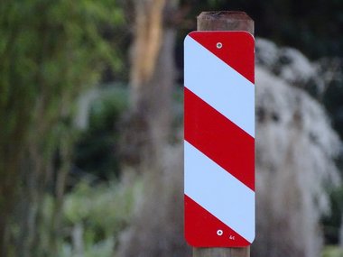 Ein längliches Schild mit rot und weißer Farbe, senkrecht an einem Pfahl befestigt mit verschwommenem Hintergrund.