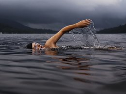 Der Kopf und ein Arm einer kraulenden Schwimmerin in einem See.