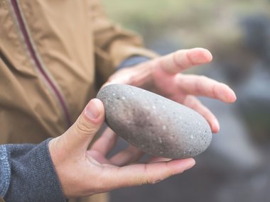 Hände halten einen runden Stein.