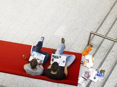 Studenten der UWH genießen eine Pause auf einem roten Sofa in einem Universitätsgebäude