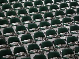 Ein Bild voller leerer, grüner, hochgeklappter Stühle mit einer Armlehne.