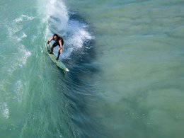 Ein Mann surft mit seinem Brett auf einer riesigen Welle.