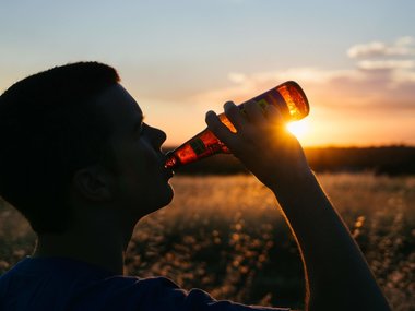 Ein Mann trinkt Bier aus einer Flasche im Abenlichtschein.
