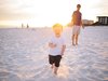 Ein kleiner Junge rennt bei Sonnenuntergang mit seinem Vater am Strand endlang.