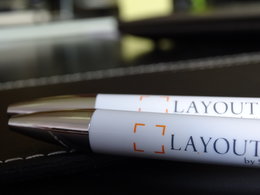 In den Metallspitzen zweier Werbekugelschreiber mit der Aufschrift "Layout" spiegelt sich das Licht einer Bürolampe.