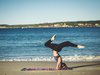Eine Frau macht einen Yogakopfstand auf einer Decke am Strand.