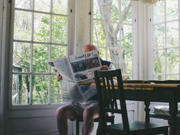 Ein Mann sitzt auf einem Stuhl und liest in einer Zeitung.