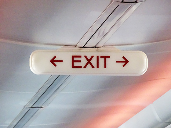 Zwei Pfeile auf einem weißen EXIT-Schild mit roter Schrift weisen nach links und rechts den Weg. Sie symbolisieren verschiedenste Wege und Reaktionen auf eine überraschende Kündigung vom Arbeitgeber. 